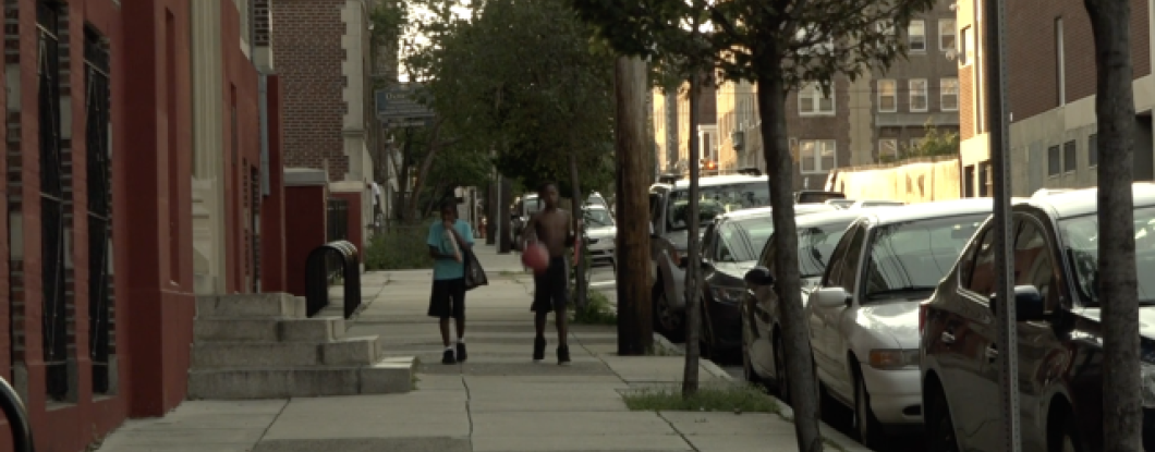 Two boys walk down a sidewalk in a residential neighborhood in Philadelphia