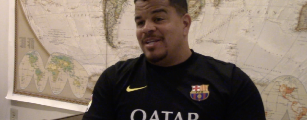 A man sits in front of a world map addressing the camera 